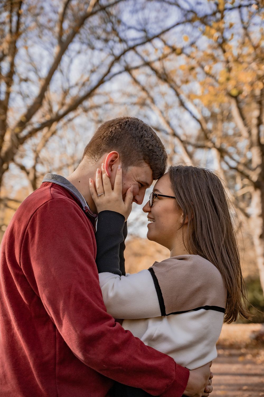 A romantic couple sharing an intimate moment on an autumn path surrounded by golden trees.