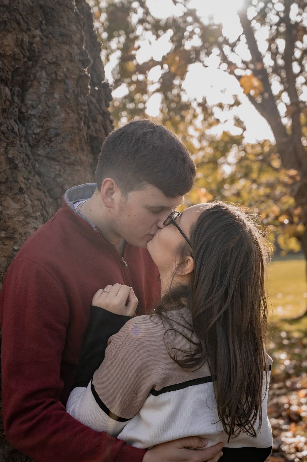 A romantic autumn moment captured between a couple near a large tree trunk with golden sunlight.