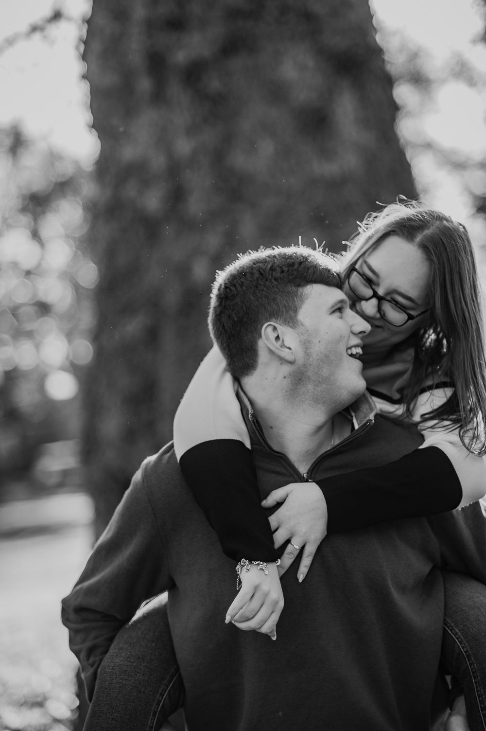 A black and white portrait of a couple sharing a joyful piggyback moment outdoors.