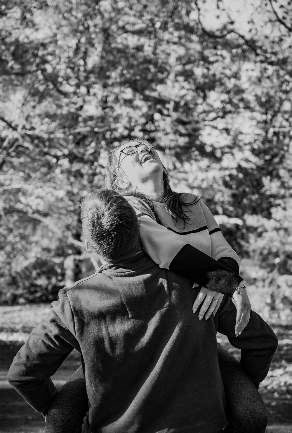 A black and white candid shot of a couple sharing a carefree laughing moment outdoors.
