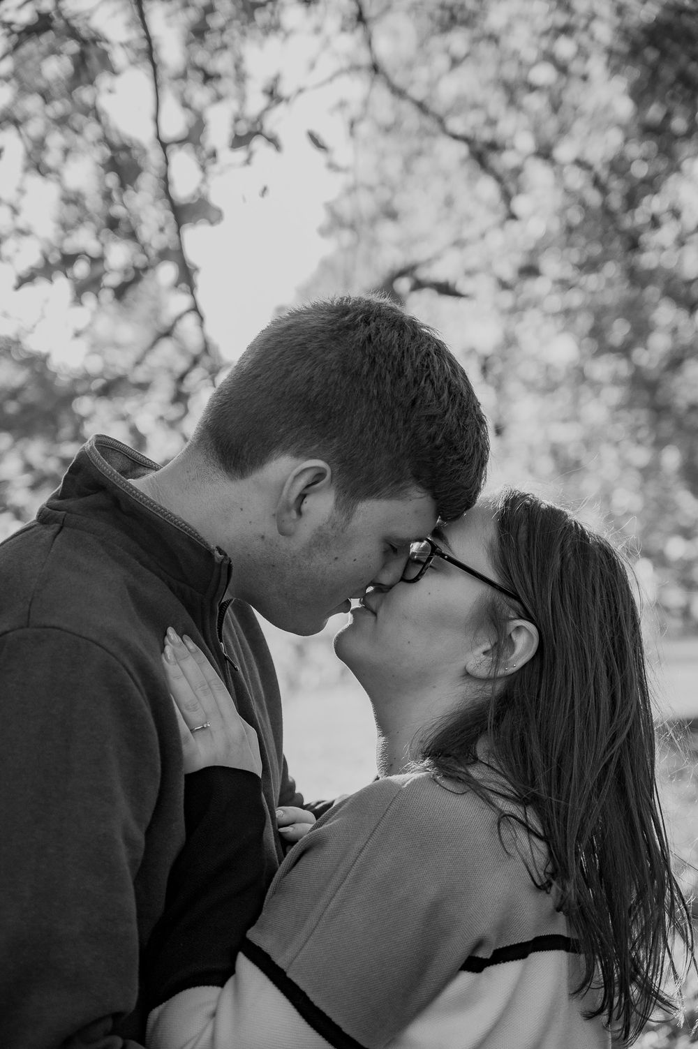 A black and white intimate portrait of a couple sharing a close moment outdoors.