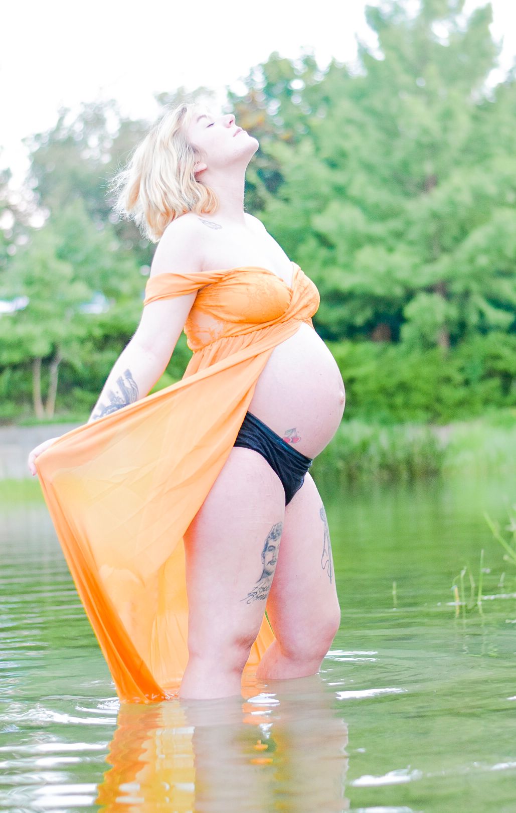 Artistic maternity photo with woman in orange dress standing in water.