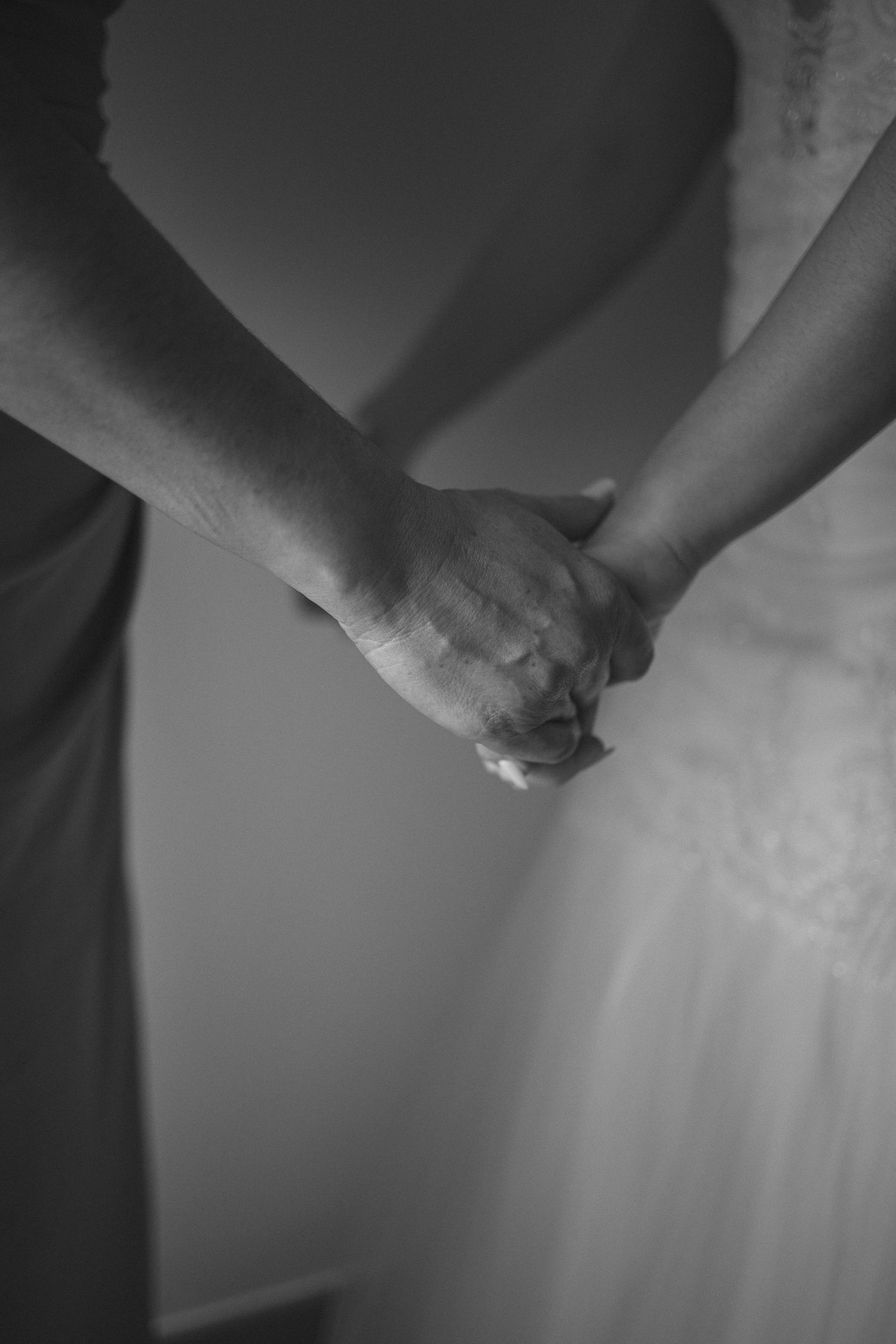 Black and white photo of two people holding hands while wearing formal dresses.