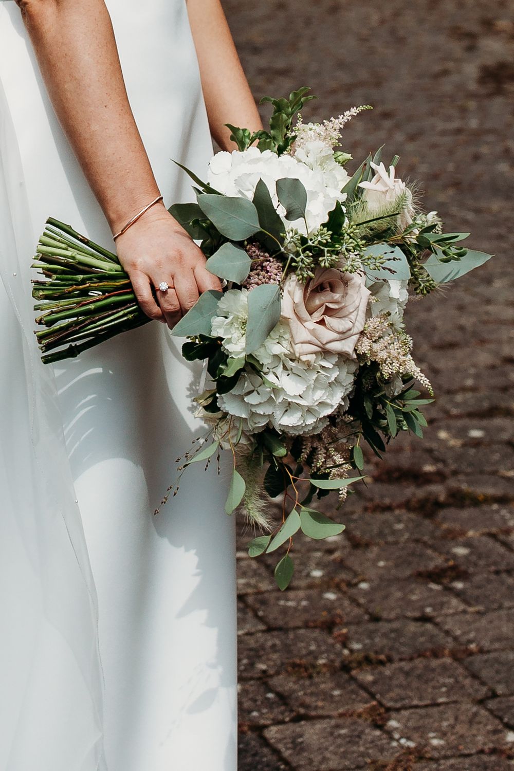 Elegant white and blush wedding bouquet with roses and eucalyptus held against white dress.