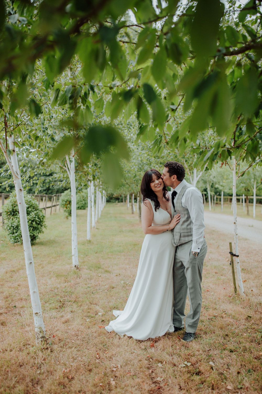 A romantic moment captured between newlyweds in an orchard with soft green foliage.