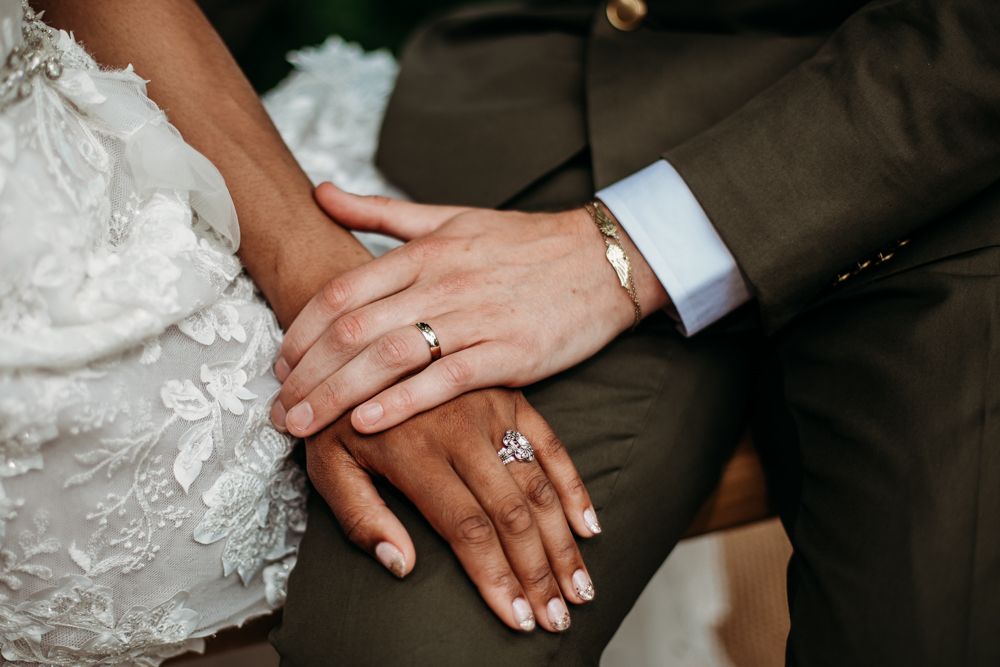 Close-up of newlyweds' hands showing wedding rings and white lace dress details.