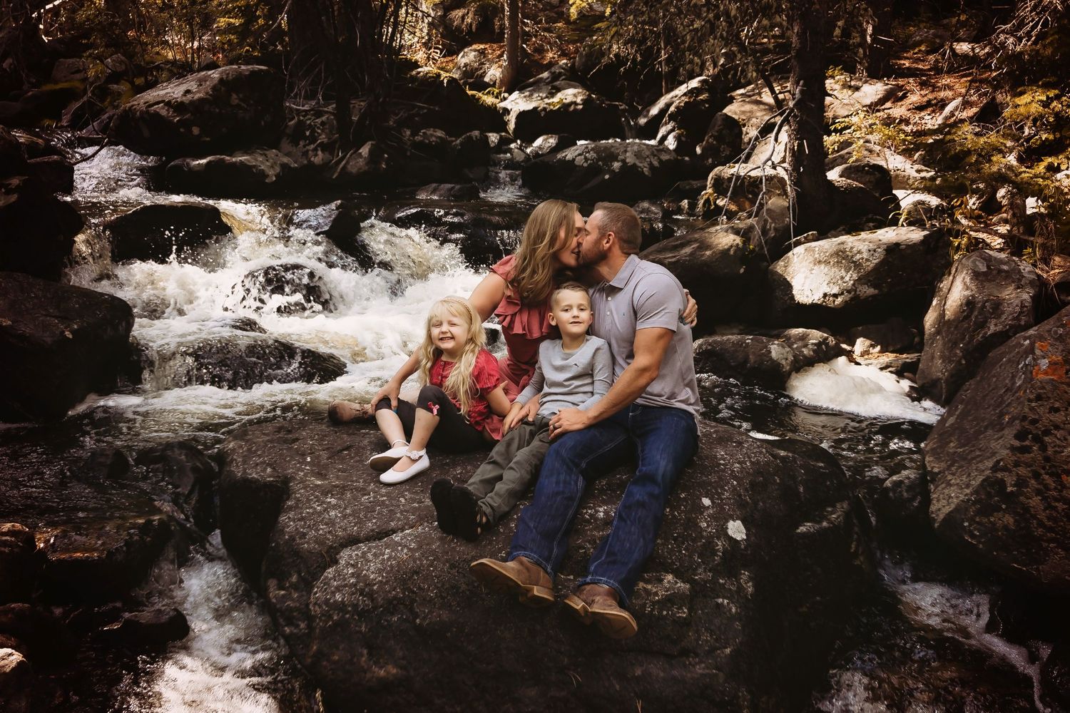 A family sits together on rocks by a cascading waterfall in a scenic outdoor setting.
