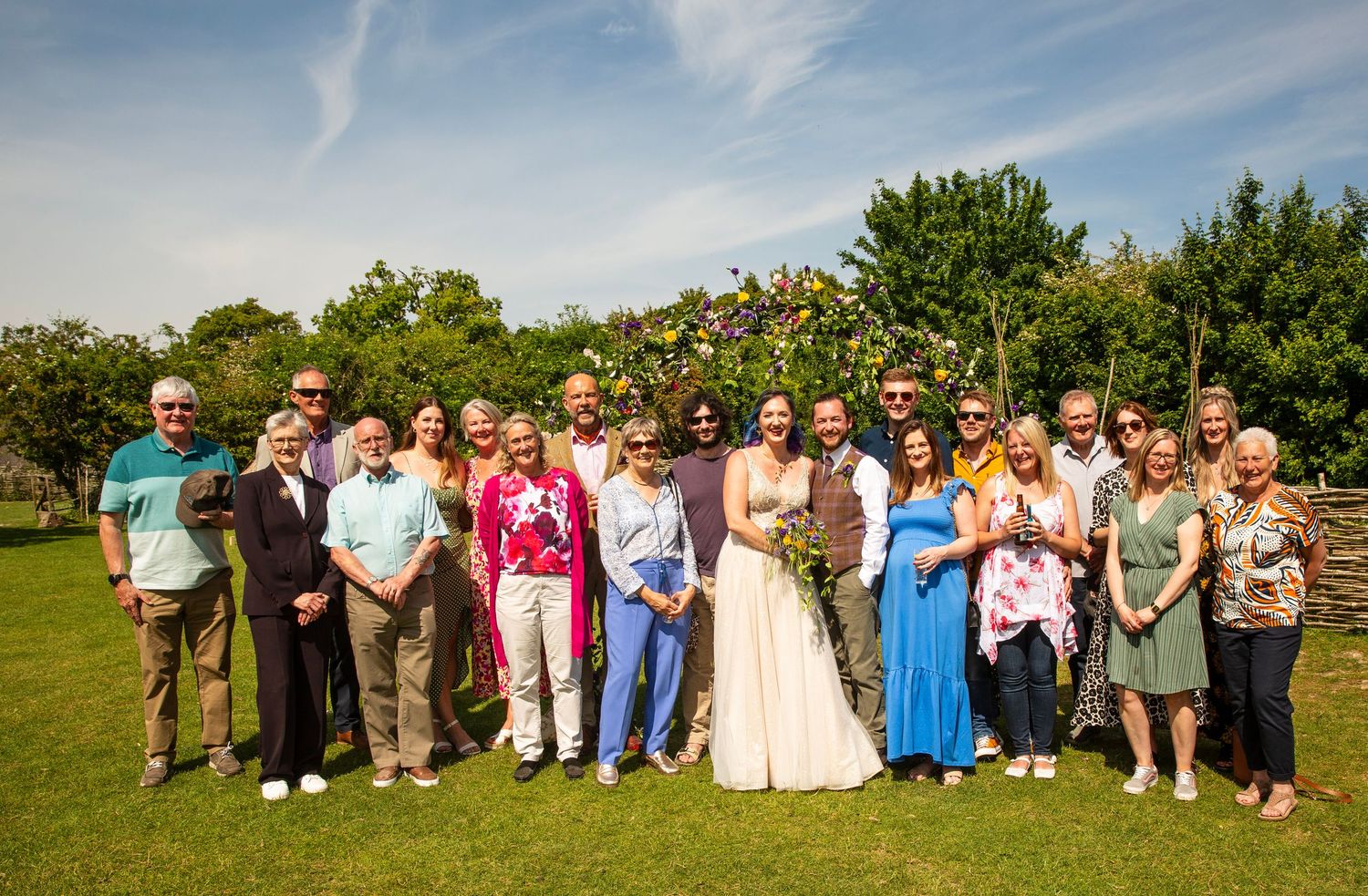 Large group photo of wedding guests posing together outdoors on a sunny day.