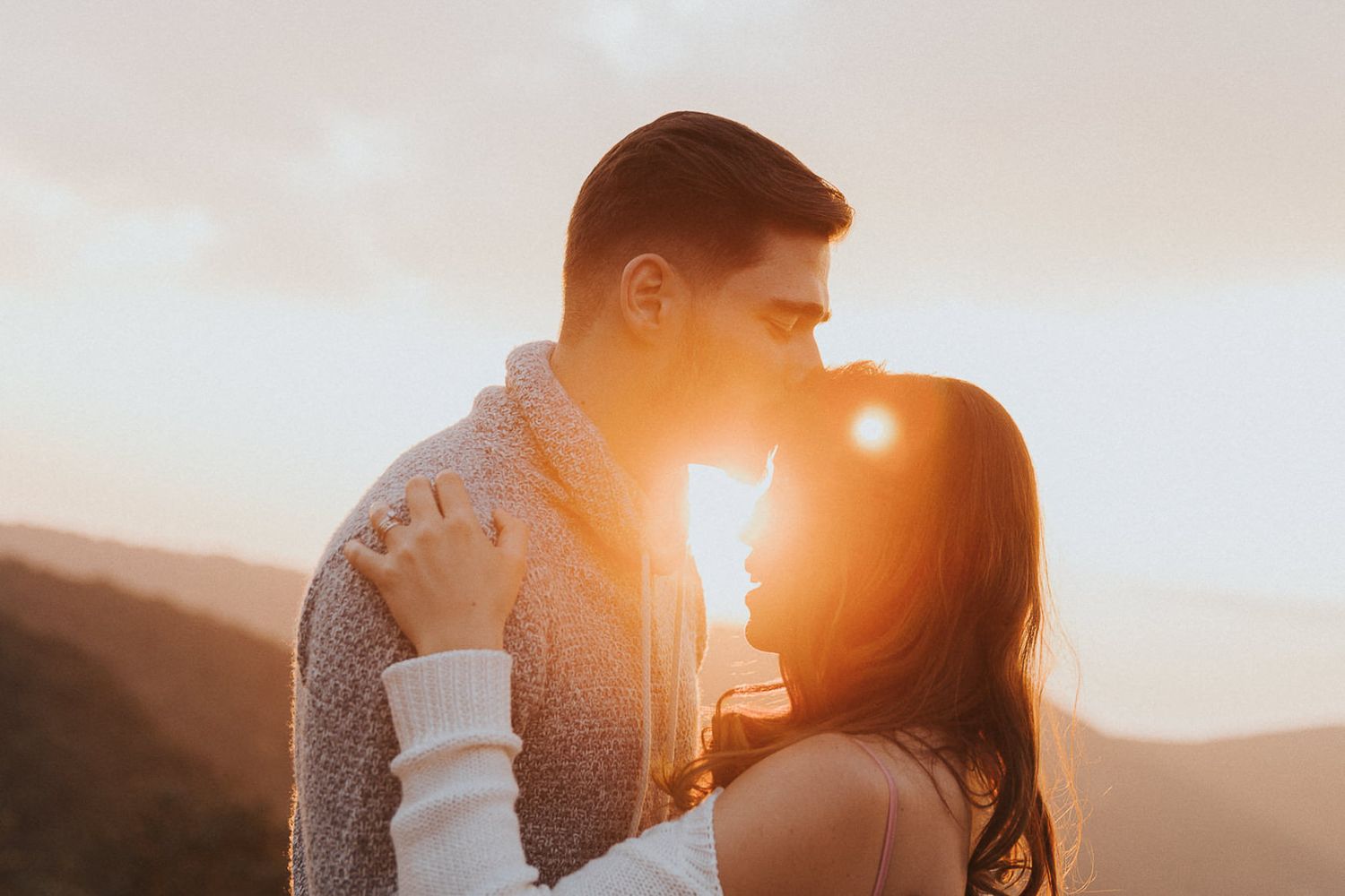 Romantic sunset silhouette of couple with sun flare creating golden glow.