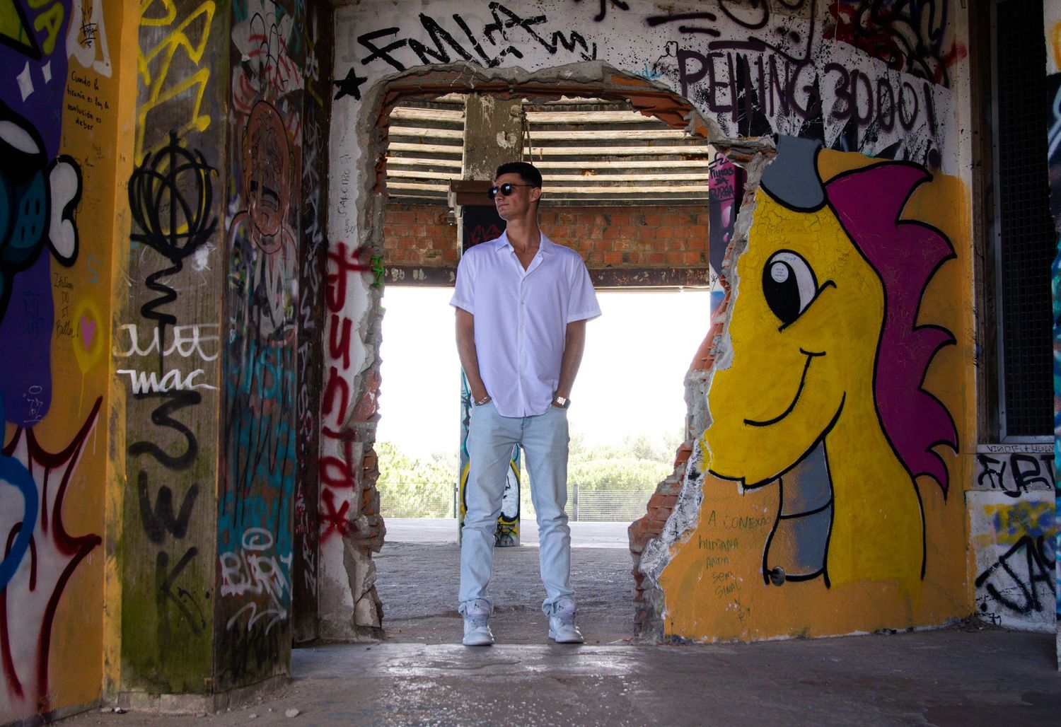 A figure stands in a graffiti-covered tunnel featuring colorful street art and a cartoon character.