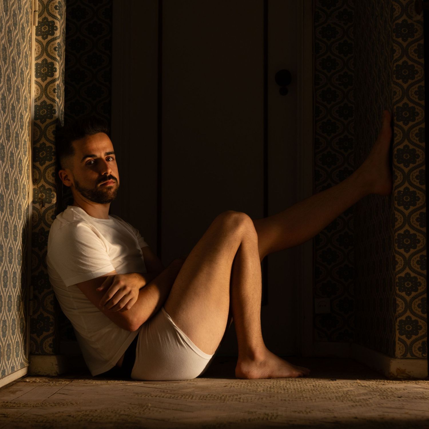 A low-light artistic portrait sitting on the floor against patterned wallpaper in warm tones.