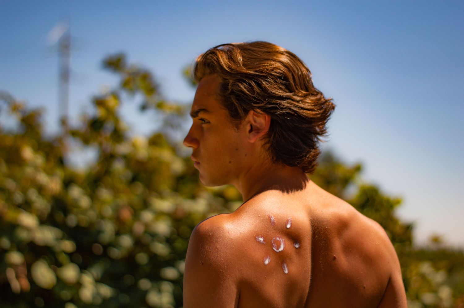 Poolside portrait against bright blue sky with wet shoulders glistening in sunlight.