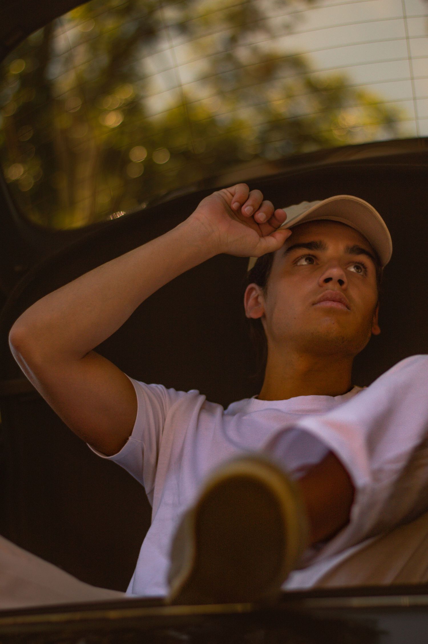 Person wearing baseball cap adjusts hat while sitting in car during golden hour.