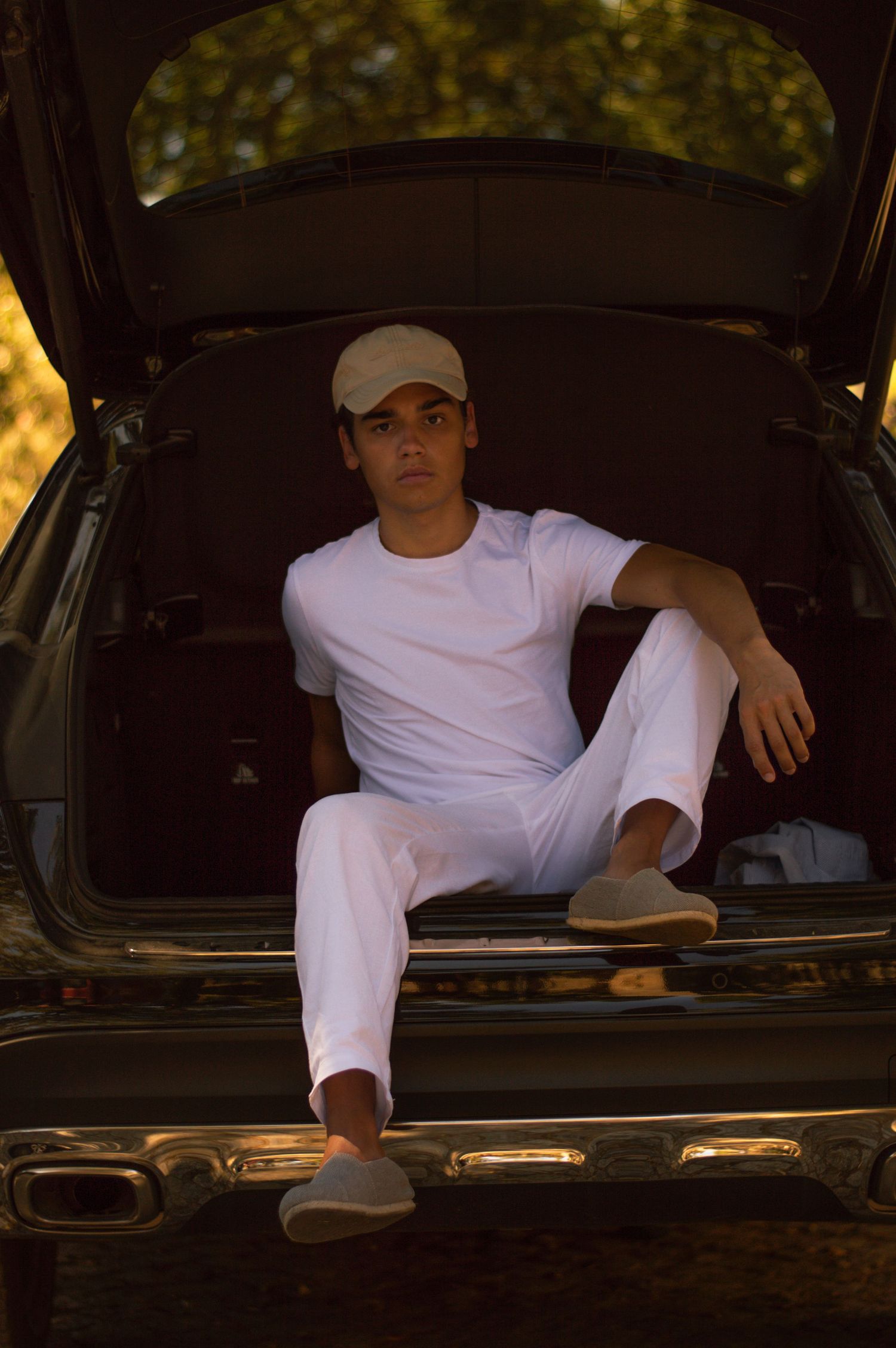 Person in white clothing reclining in back of dark car with natural lighting.
