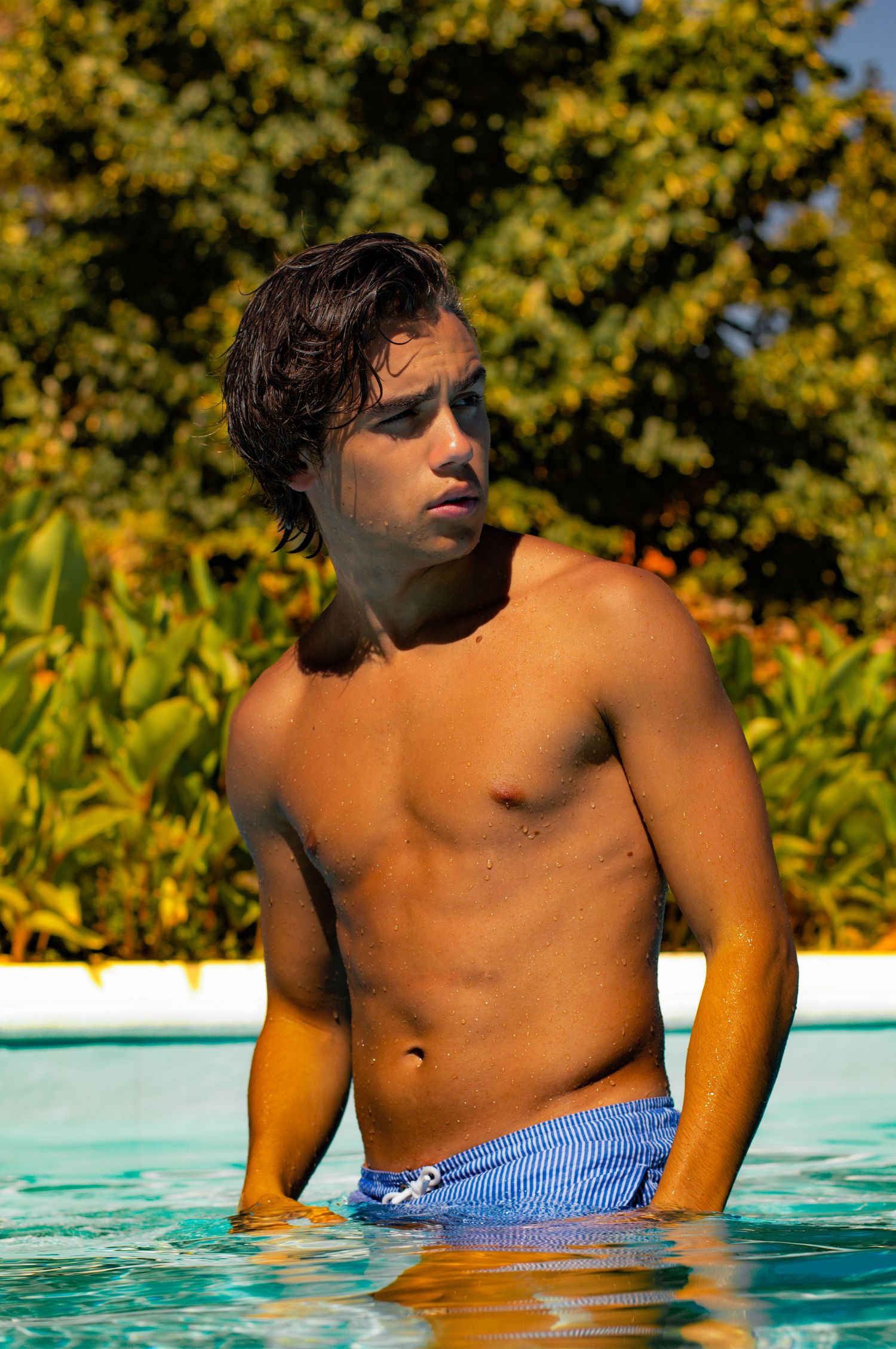 Figure lounging in blue swimming pool with lush yellow foliage in background.