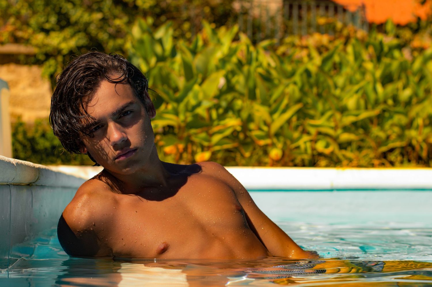 Person lounging by pool edge during golden hour with lush greenery in background.