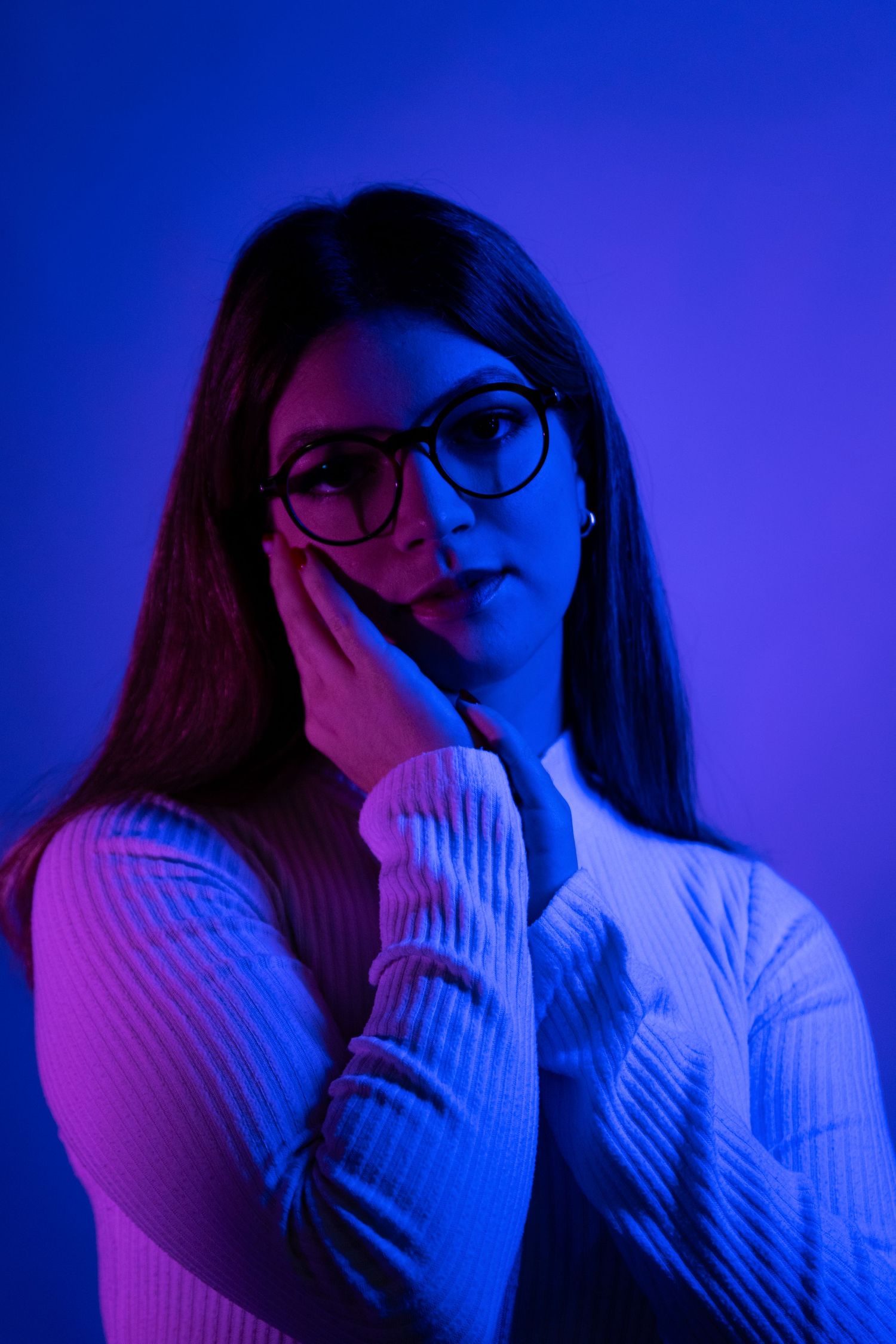 Moody portrait in white turtleneck with hand gesture against blue lighting.