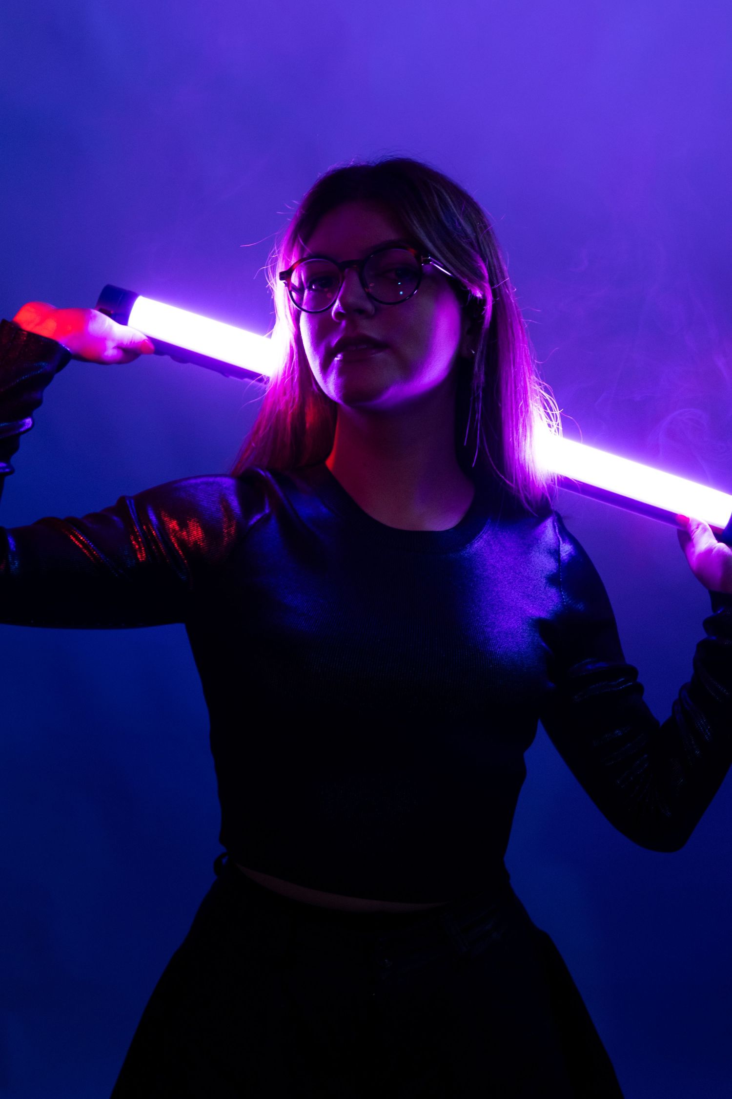 Silhouette holding glowing neon light sticks against purple background.