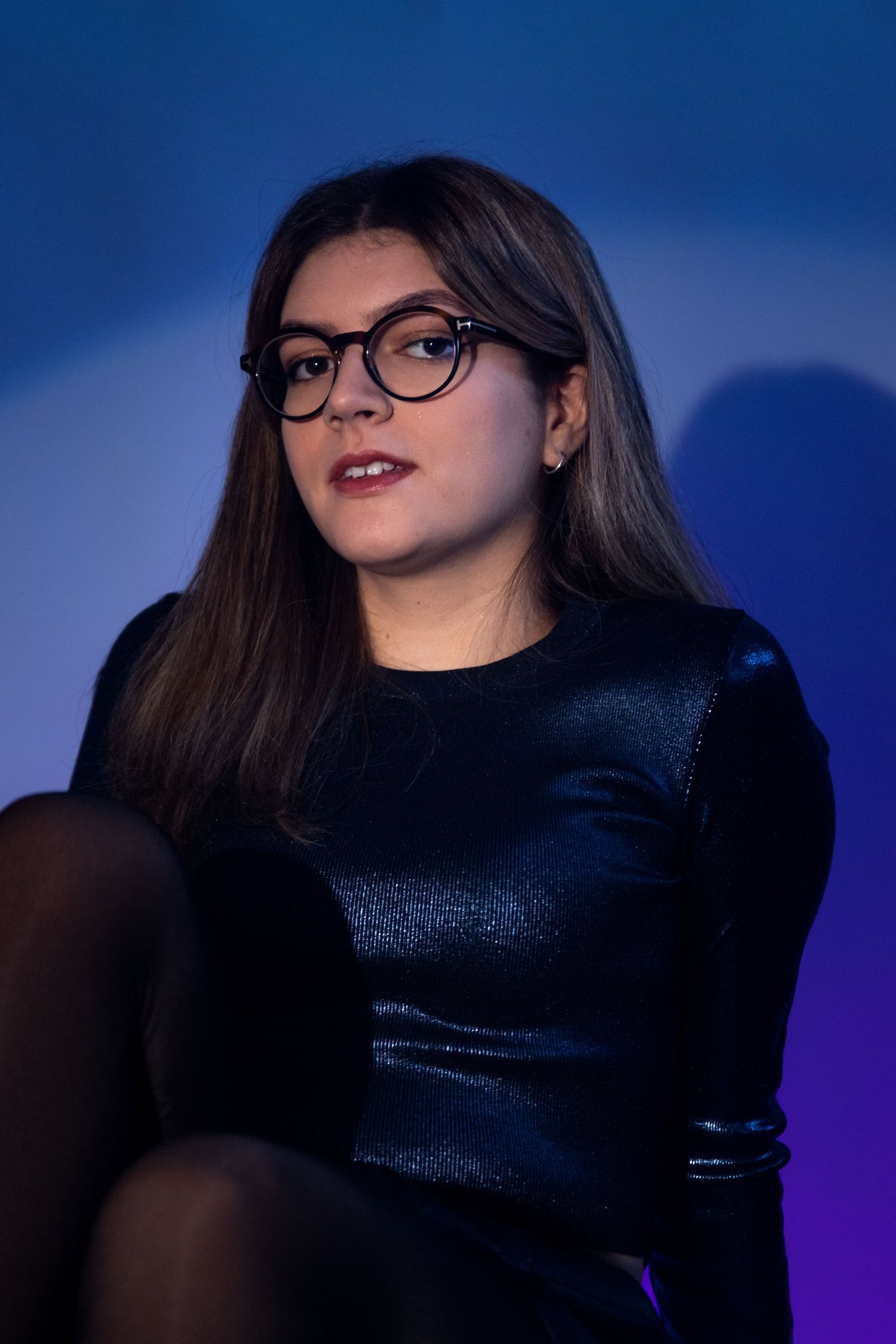 Fashion portrait in black shimmering top against blue-purple gradient lighting.