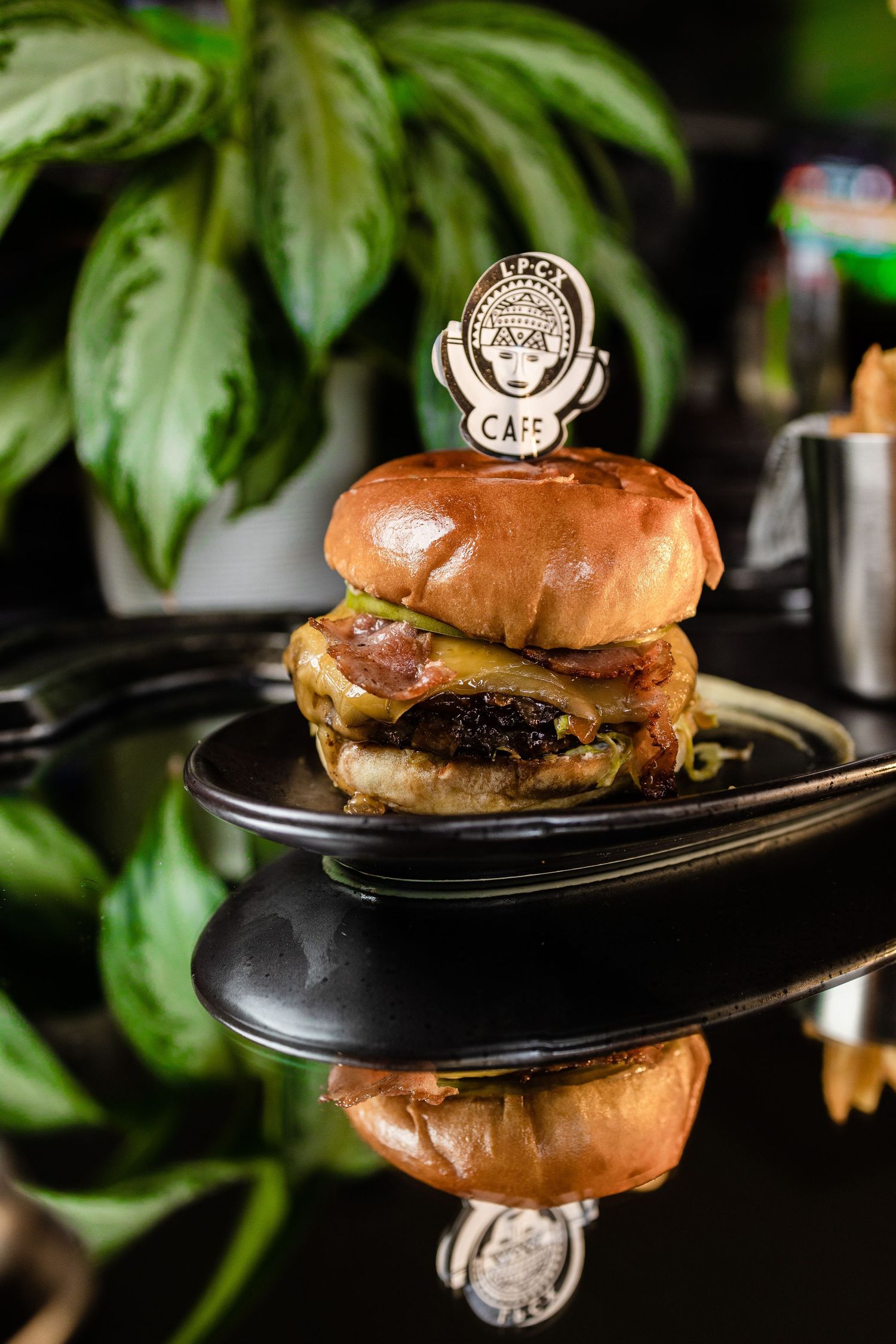 Juicy gourmet burger with melted cheese on black plate reflecting restaurant logo.