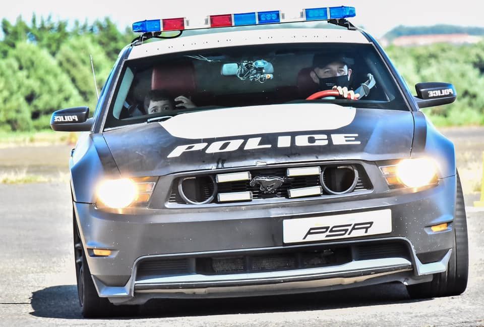 Gray police car with flashing red and blue lights on rural road.
