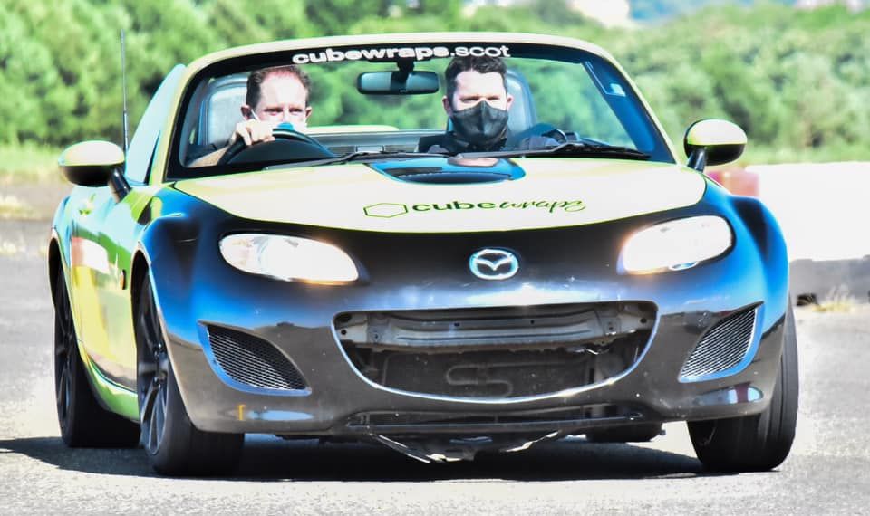 Blue Mazda MX-5 sports car on racetrack.
