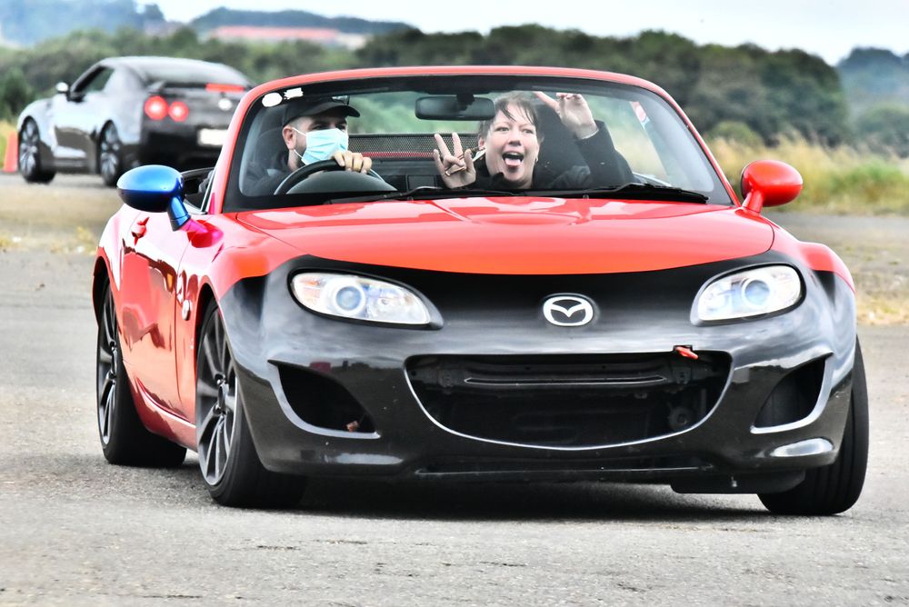 Red Mazda MX-5 convertible driving on rural road.