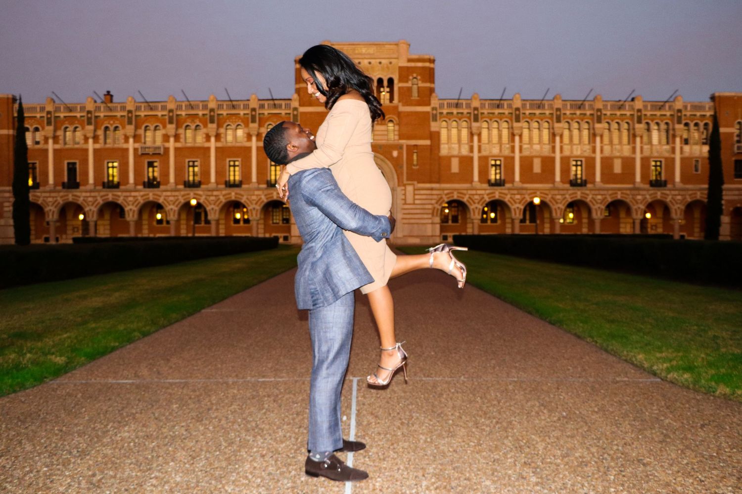 Romantic sunset engagement portrait with couple embracing in front of historic building.