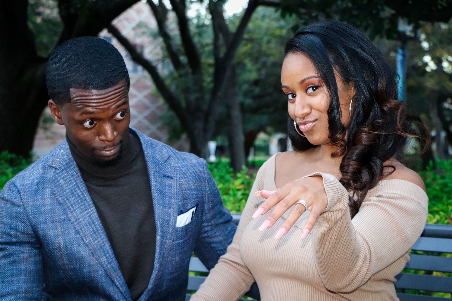 Engaged couple sitting on park bench showing off engagement ring in outdoor engagement photo session.