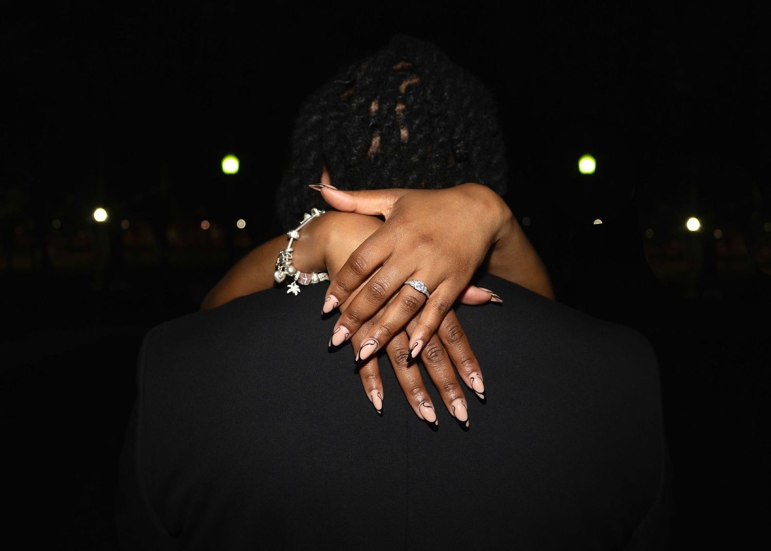 Close-up of manicured hands with jewelry against dark background.