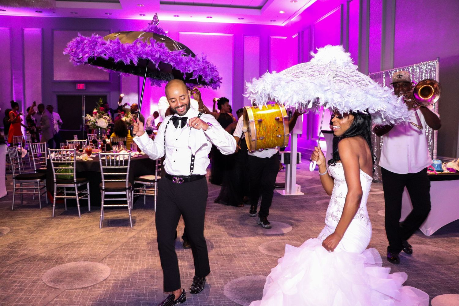 Reception celebration with dancing and decorative umbrellas under purple mood lighting.