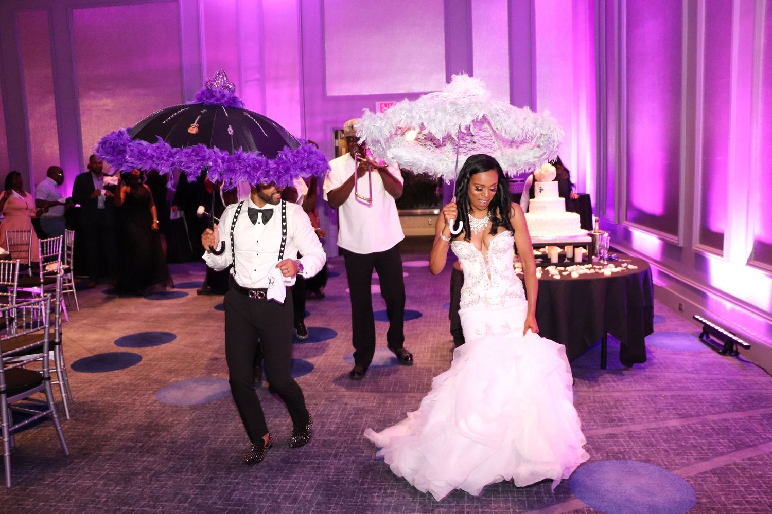 Wedding reception scene with guests dancing under purple lighting holding decorative umbrellas.