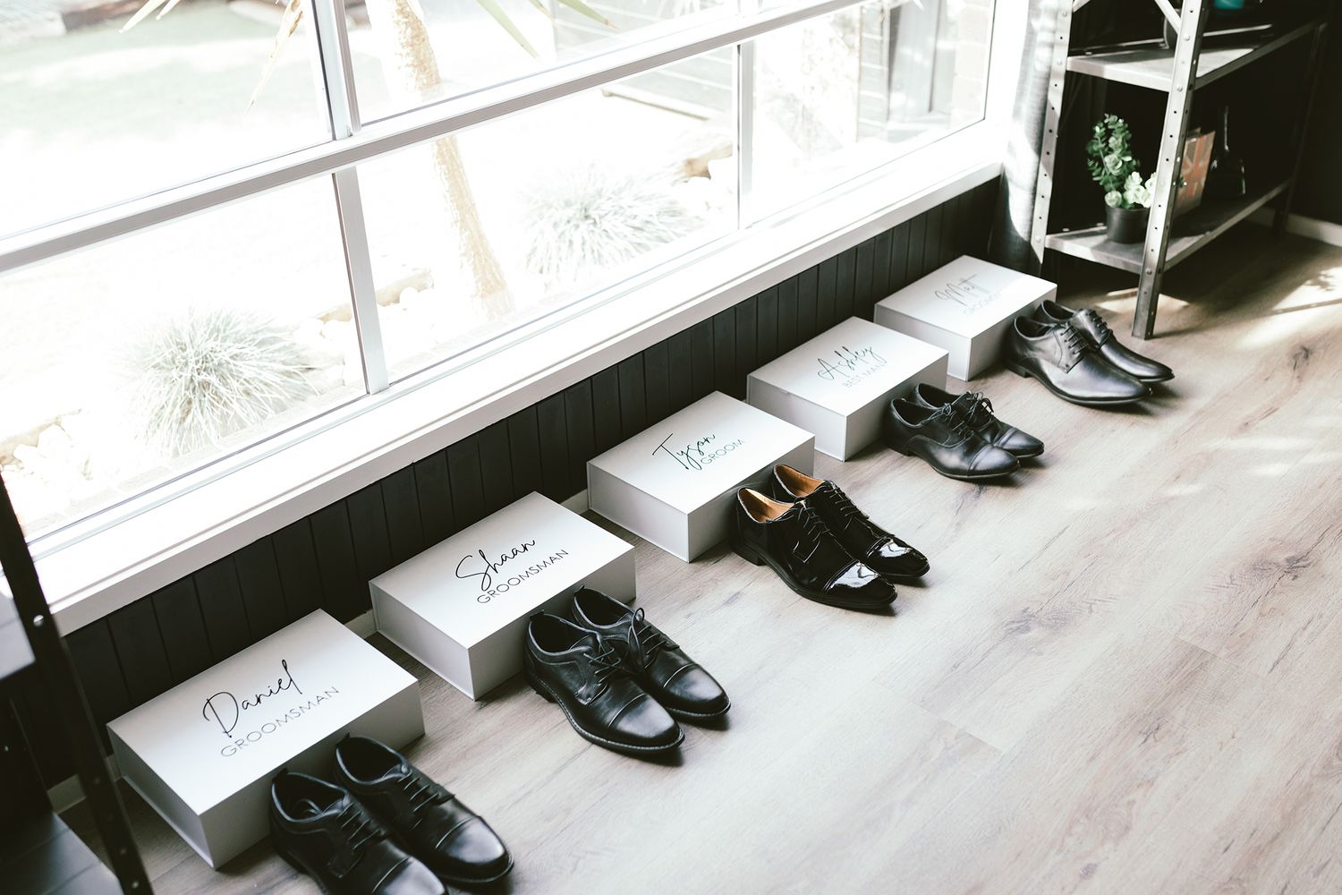 Row of formal black dress shoes displayed beneath window with name cards for groomsmen.