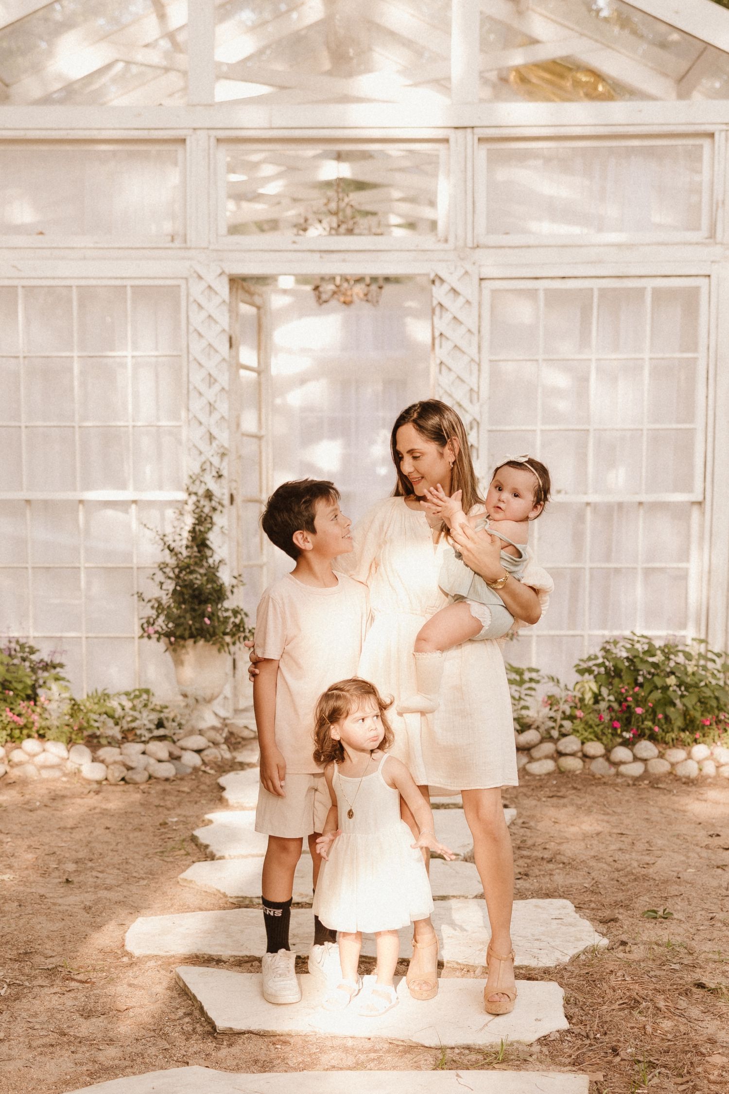 Family portrait in sunlit greenhouse with stone pathway and natural lighting.