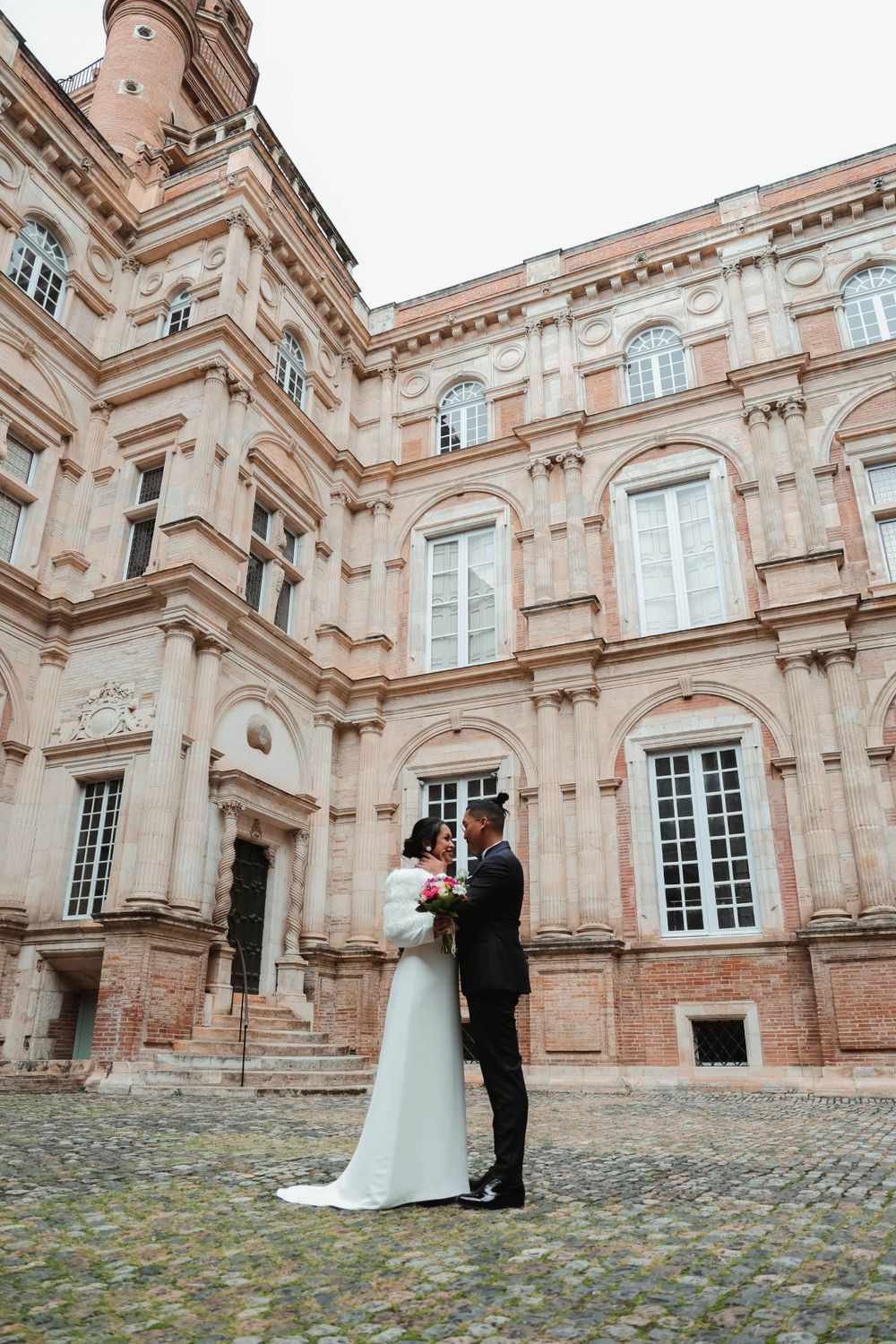A wedding couple poses outside a grand historic building with ornate architecture.