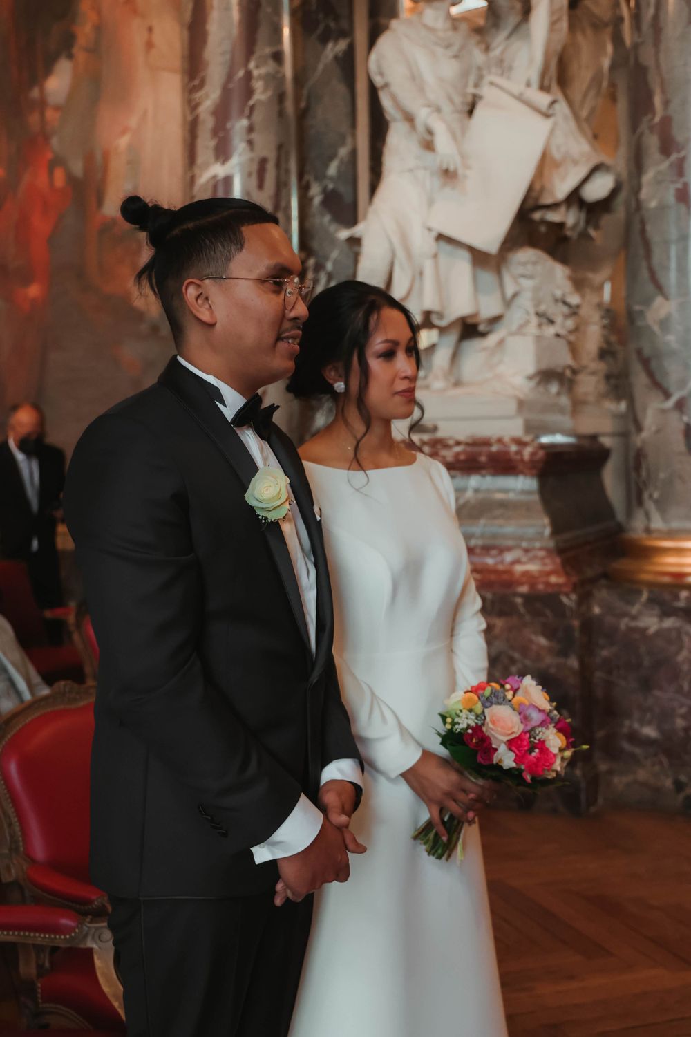 A couple in elegant wedding attire poses together against dramatic interior architecture.