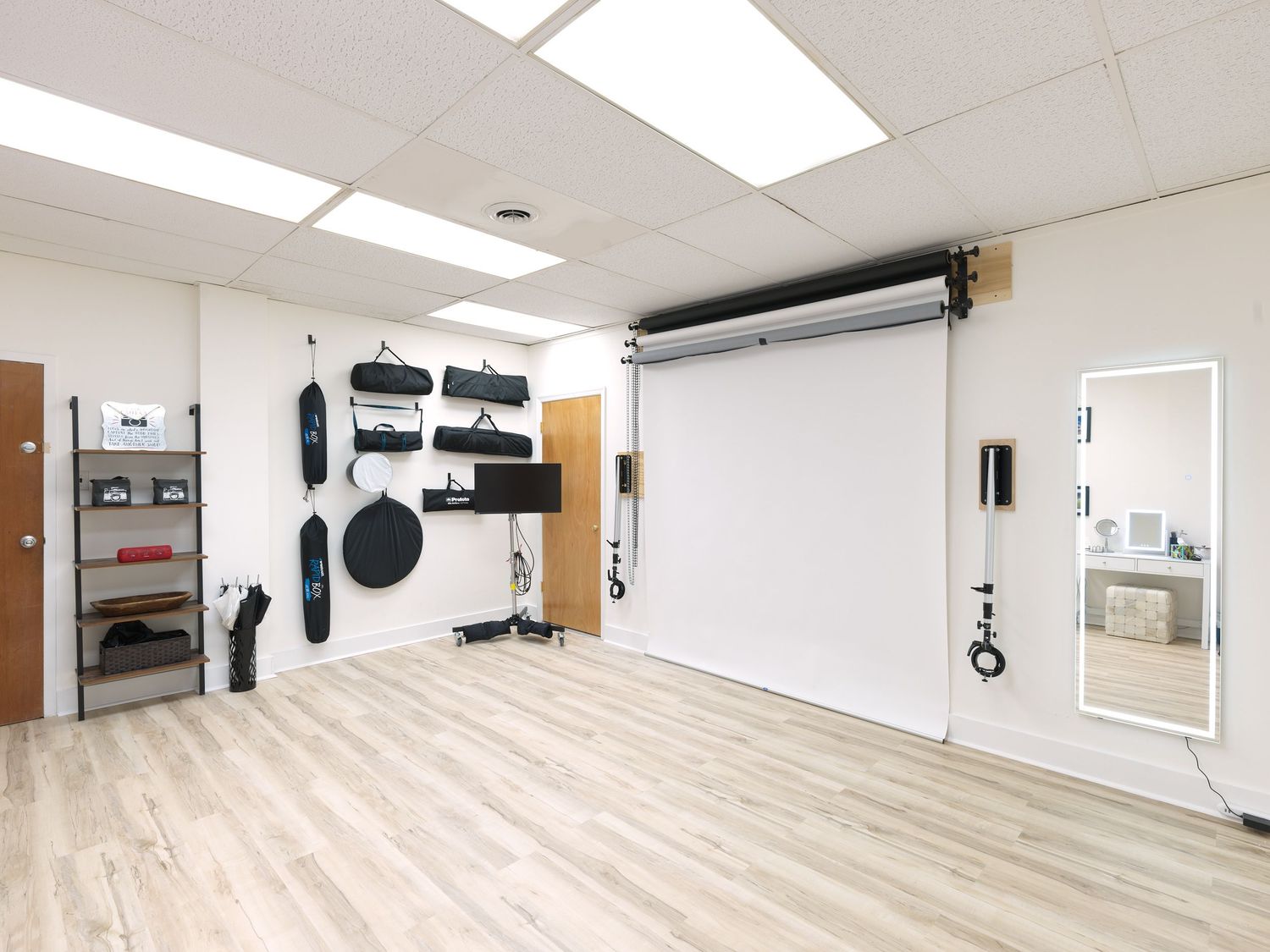 Professional photo studio interior with white backdrop, lighting equipment, and wood flooring.