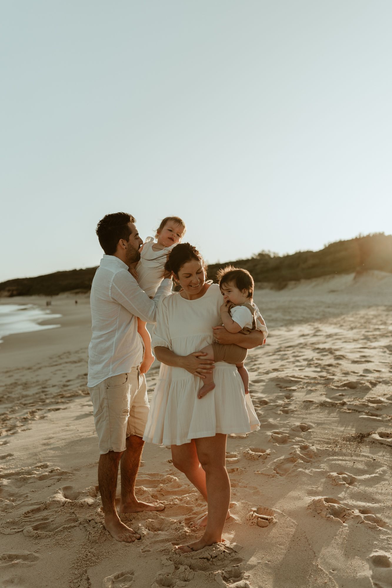 A family shares laughter and embraces on a beach during golden hour.