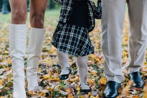 Close-up of family feet standing on fallen autumn leaves, child in plaid dress between parents.