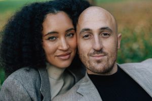 Close portrait of interracial couple leaning together smiling in a green field.