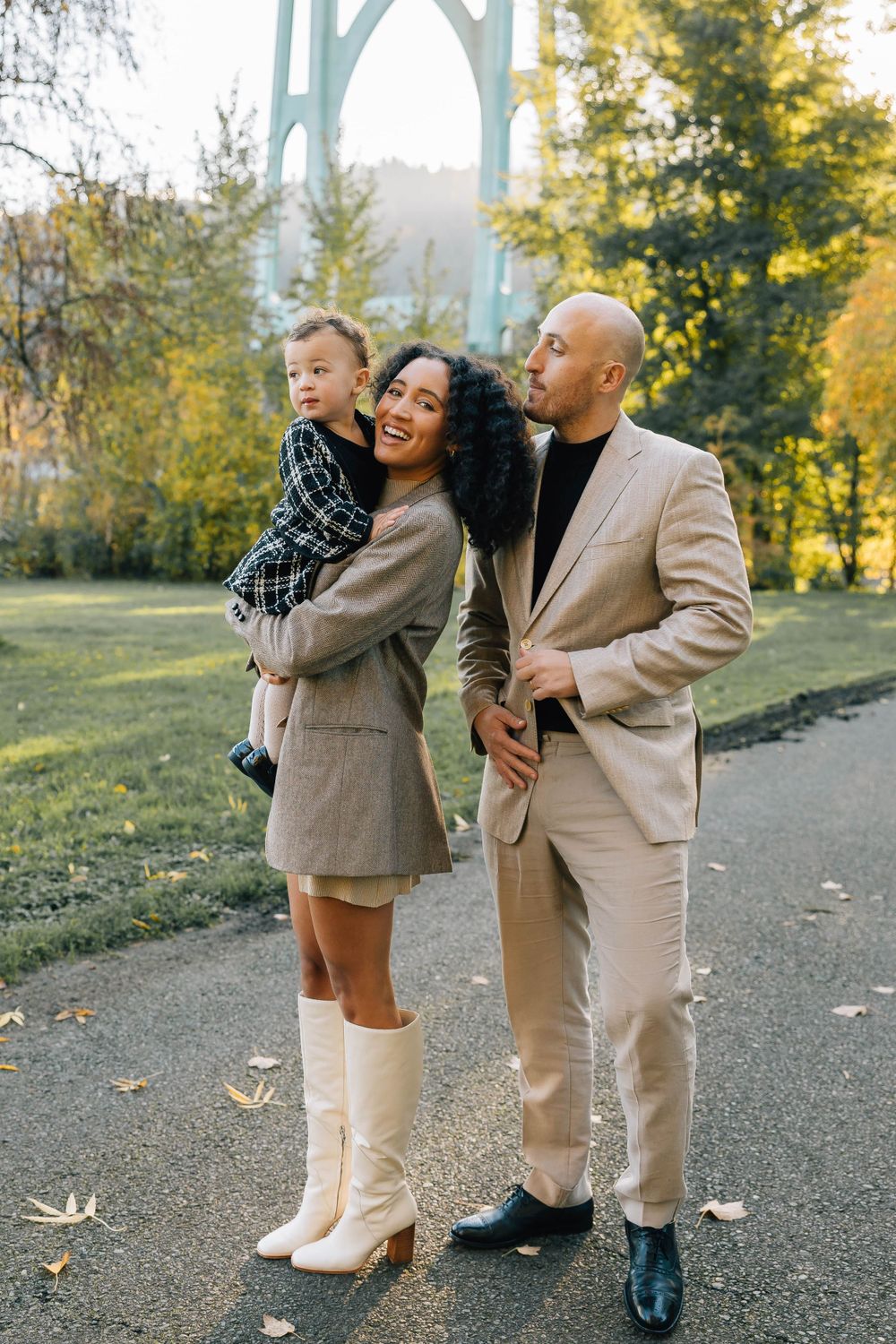 A happy mixed-race family with a toddler poses together in a park during fall, dressed in elegant neutral tones.