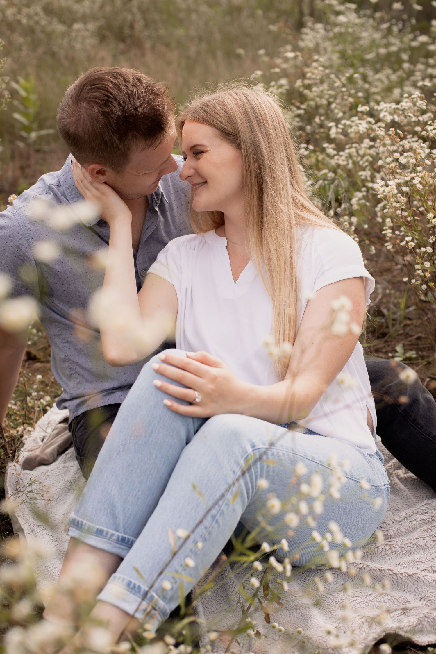 A couple shares an intimate moment while sitting among wildflowers in casual attire.