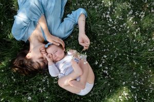 Sioux City, Iowa photographer. Mother lying on grass with baby, sharing a tender moment outdoors among wildflowers.