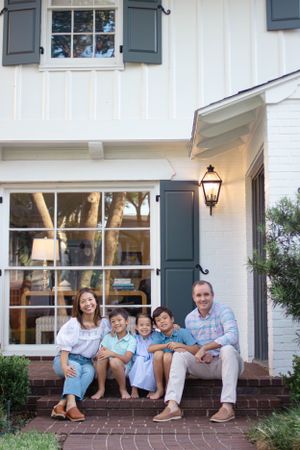 Sioux City, Iowa photographer. Happy blended family of five posing on brick steps outside white home with dark shutters at dusk.