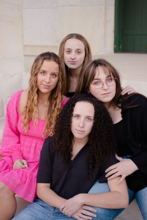 Sioux City, Iowa photographer. Four teenage girls posing together for a group portrait outdoors against a light stone wall background.