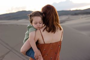 Sioux City, Iowa photographer. Mother holding young child from behind on sandy desert dunes during warm golden sunset photography session.