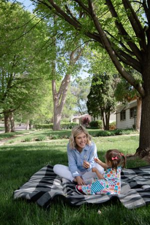 Sioux City, Iowa photographer. Smiling grandmother sitting on a blanket with her toddler daughter under green trees in a park.