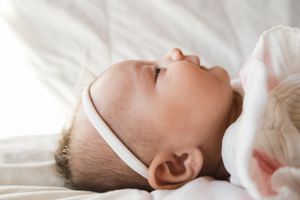 Sioux City, Iowa photographer. Peaceful newborn baby lying on white blanket with soft natural light, wearing a white headband.