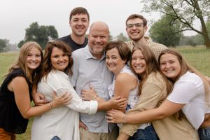 Sioux City, Iowa photographer. Extended family of nine smiling and hugging outdoors in a green field.