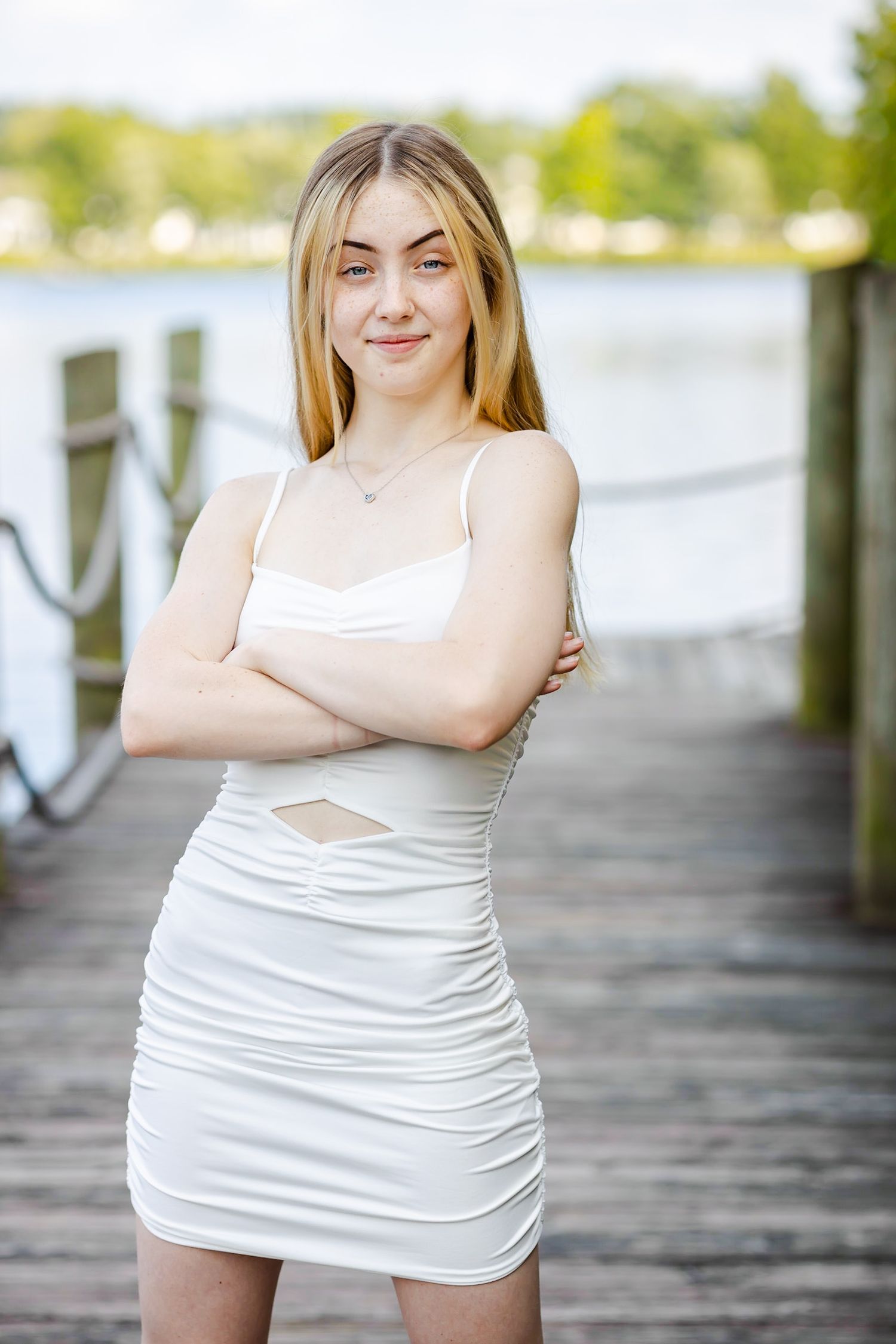 Person in white ruched dress standing on wooden dock near water.